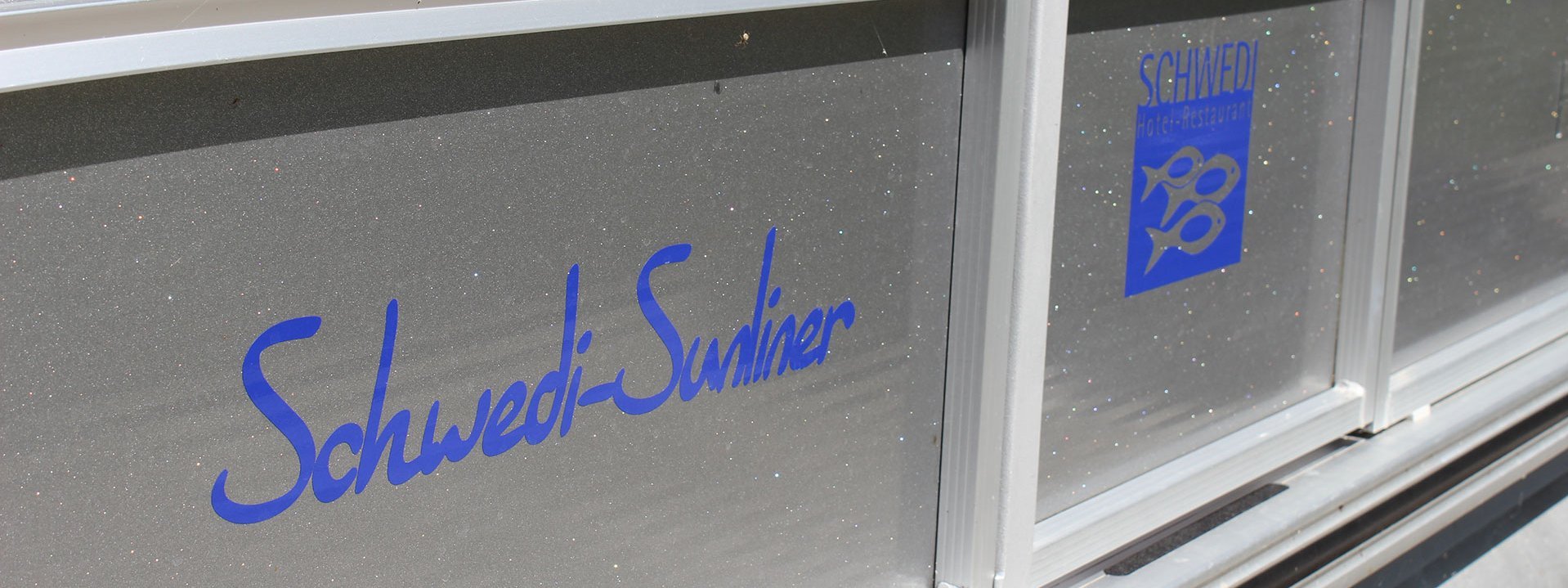 Auf dem Bild sind Fenster zu sehen, auf denen der Schriftzug "Schwedi-Sunliner" und das Logo des Hotel Schwedi zu sehen sind.