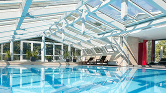 Modernes Hallenbad mit Glasdach im Hotel Schwedi – lichtdurchfluteter Wellnessbereich mit Blick ins Grüne.