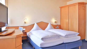 Kompaktes Doppelzimmer im Hotel Schwedi mit Holzmöbeln, Fernseher und gemütlicher Einrichtung.