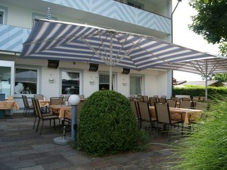 Sonnenterrasse des Hotel Schwedi mit beschatteten Sitzplätzen, Markisen und gepflegter Bepflanzung – ideal für Frühstück oder Abendessen im Freien.