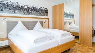 Franzl Suite Schlafzimmer der Franzl Suite im Hotel Schwedi mit Doppelbett, großem Kleiderschrank und modernem Wandbild – komfortabel wohnen mit stilvollem Design.