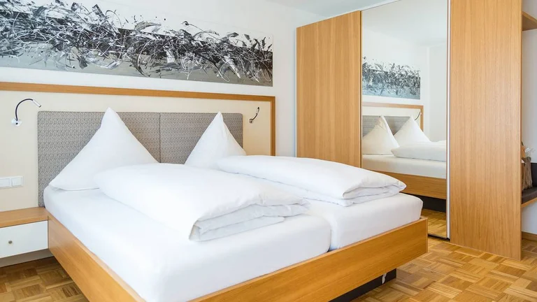 Schlafzimmer der Franzl Suite im Hotel Schwedi mit Doppelbett, großem Kleiderschrank und modernem Wandbild – komfortabel wohnen mit stilvollem Design.