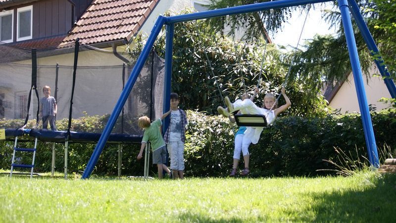 Vier Kinder spielen im Garten des Hotel Schwedi. Ein Junge ist auf dem Trampolin, ein Mädchen schaukelt und zwei Jugend stehen neben dem Trampolin.