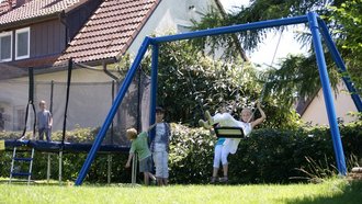 Spielplatz im Gartenbereich des Hotel Schwedi mit Schaukel, Trampolin und spielenden Kindern – familienfreundliche Atmosphäre für Urlaub mit Kindern.
