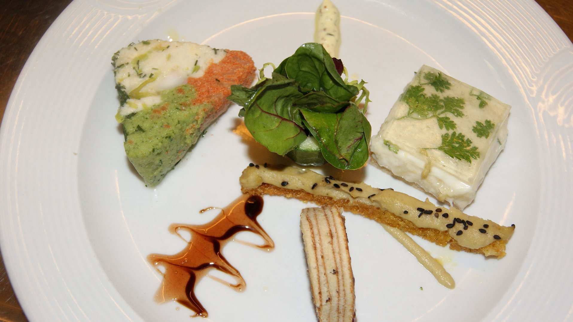 Eine Variation von verschiedenem Gemüse und Fisch ist auf einem weißen Teller kunstvoll drapiert. 