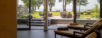 Ruhebereich im Wellnessbereich des Hotel Schwedi mit Relaxliegen, bodentiefen Fenstern und Ausblick in den Garten mit Sitzterrasse und Bodenseepanorama.
