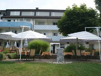 Blick auf die Terrasse und das Hauptgebäude des Hotel Schwedi mit Sonnenschirmen, Sitzgruppen und gepflegtem Garten – einladender Außenbereich für Gäste.

