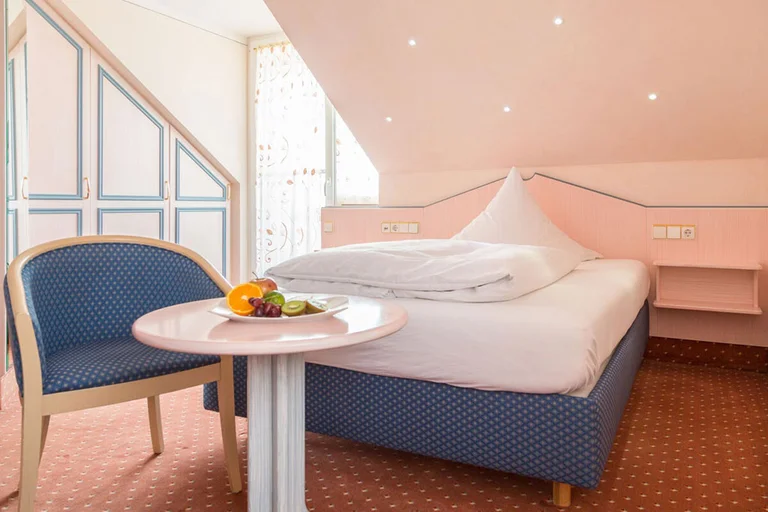 Einzelzimmer im Hotel Schwedi mit gemütlichem Bett, pastellfarbenem Mobiliar und Sitzgelegenheit unter der Dachschräge – charmanter Rückzugsort mit individuellem Stil.
