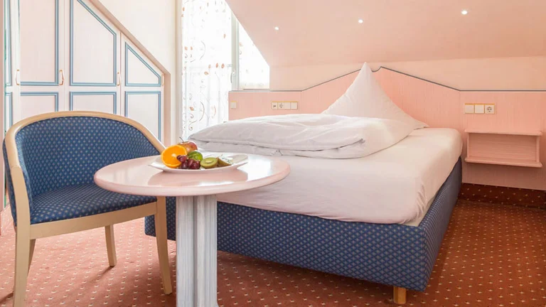Einzelzimmer im Hotel Schwedi mit gemütlichem Bett, pastellfarbenem Mobiliar und Sitzgelegenheit unter der Dachschräge – charmanter Rückzugsort mit individuellem Stil.