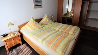 Schlafzimmer einer Ferienwohnung im Hotel Schwedi mit Doppelbett, Nachttischlampe und geräumigem Spiegelschrank – gemütliche Atmosphäre für erholsamen Schlaf.