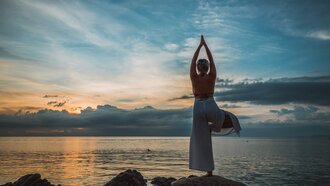 Frau steht auf Steinen am See und macht Yoga