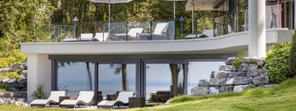 Modernes Wellnessgebäude des Hotel Schwedi mit zwei Ebenen, Sonnenterrasse, Liegestühlen und Glasfassade – Entspannung inmitten grüner Natur mit Seeblick.