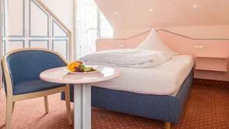Einzelzimmer im Hotel Schwedi mit gemütlichem Bett, pastellfarbenem Mobiliar und Sitzgelegenheit unter der Dachschräge – charmanter Rückzugsort mit individuellem Stil.