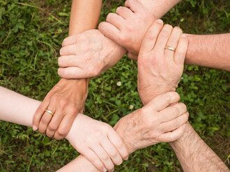 Hände unterschiedlicher Menschen greifen ineinander und bilden einen Kreis – Symbol für Zusammenhalt, Vielfalt und Teamgeist im Hotel Schwedi.