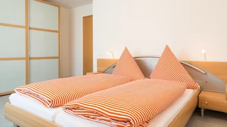 Modernes Schlafzimmer einer Ferienwohnung im Hotel Schwedi mit Doppelbett, großem Schiebetürenschrank und grafischer Bettwäsche – freundlich, hell und funktional gestaltet.