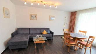 Wohnzimmer einer Ferienwohnung im Hotel Schwedi mit Ecksofa, Essbereich und viel Tageslicht – großzügiger Raum für entspannte Urlaubstage.