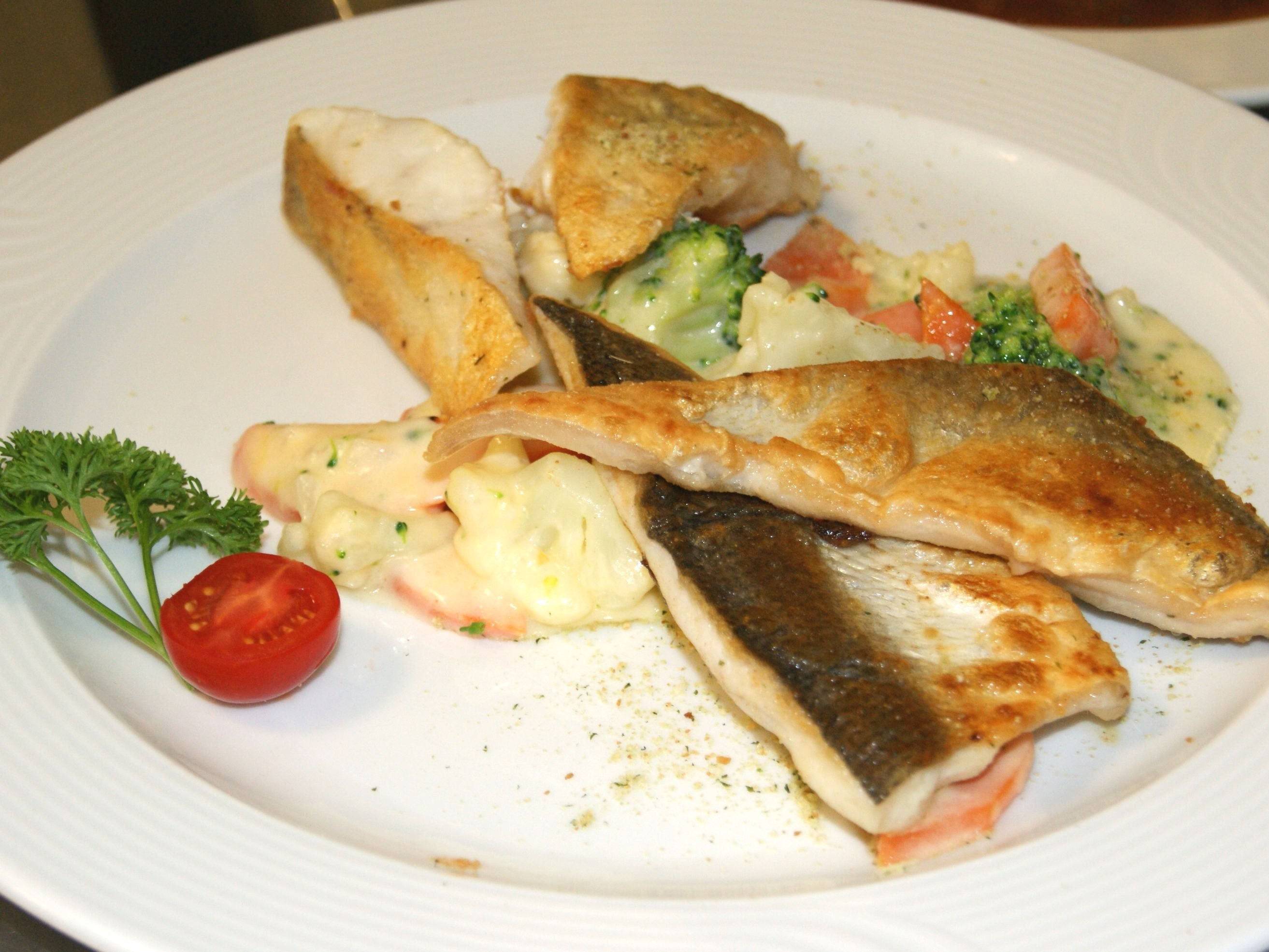 Verschiedene Fischfiletstücke liegen auf einem Teller mit buntem Gemüse