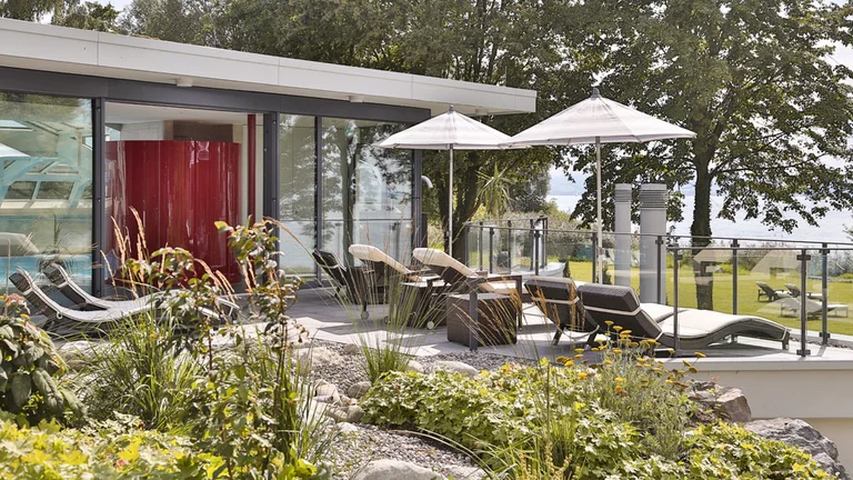 Sonnenterrasse des Wellnessbereichs im Hotel Schwedi mit Liegestühlen, Sonnenschirmen und Blick ins Grüne – entspannen in naturnaher Ruhezone am Bodensee.