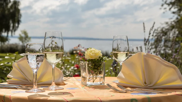 Festlich gedeckter Tisch mit Blick auf den Bodensee im Garten des Hotel Schwedi – stilvolles Outdoor-Dinner mit Weißwein und Blumenarrangement.